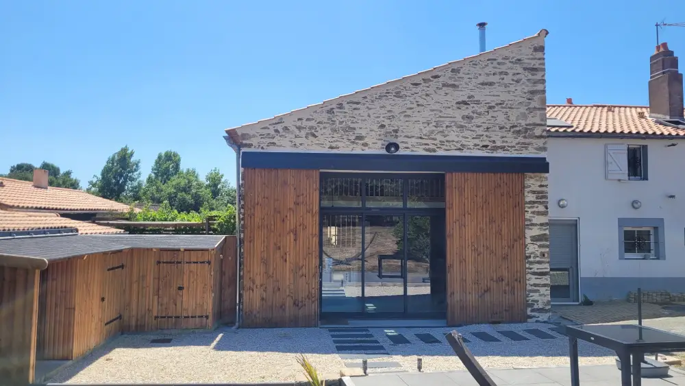 les pierres apparentes de la façade principale de la grange ont été conservées et enduites. Le portail métallique a été remplacé par une grande baie vitrée avec des volets coulissants en bois massif